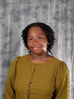 College-aged female student, dark hair, loc'd, medium length hair, dark eyes, green long-sleeve blouse with buttons, wearing earrings