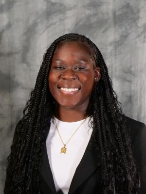 College-age female student, dark hair, long hair in boho braids, wearing a white shirt covered with a black blazer, smiling with teeth