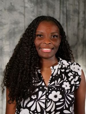 College-aged female student. Dark medium length boho braids. Dark eyes. Smiling with teeth. Black short sleeve button up blouse with white floral print. Diamond earrings.