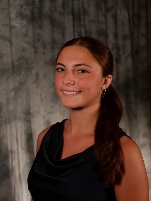 College-aged female student. Brown hair, pulled back into ponytail, slightly forward. Dark eyes. Smiling with teeth. Gold earrings. Black sleeveless blouse.