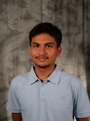 College-aged male student. Dark short hair. Dark eyes. Facial hair. Light blue polo.