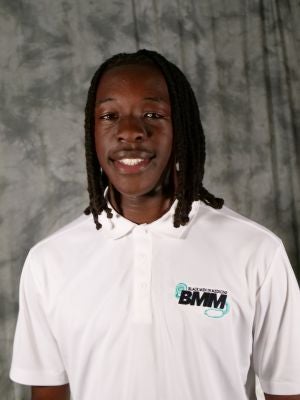 College-aged male student. Dark, shoulder-length locs in a twist style. Smiling with teeth. White polo with a Black Men in Medicine logo.