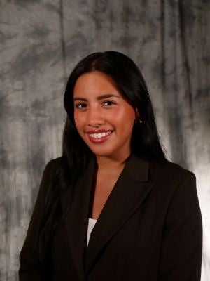 College-aged female student, dark long hair, dark eyes, smiling with teeth, white shirt, black blazer covering shirt