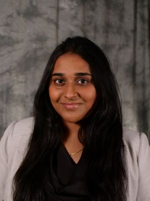 College-aged female student, dark long hair, dark eyes, smiling, black blouse with white blazer, gold necklace