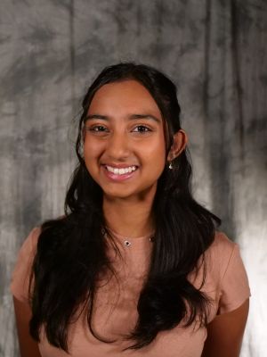 College-aged female student, dark hair half-up with hair in front, dark eyes, smiling with teeth, pink blouse, earrings