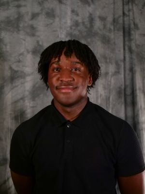 College-aged male student, dark hair, two-strand twist, dark eyes, smiling, black polo