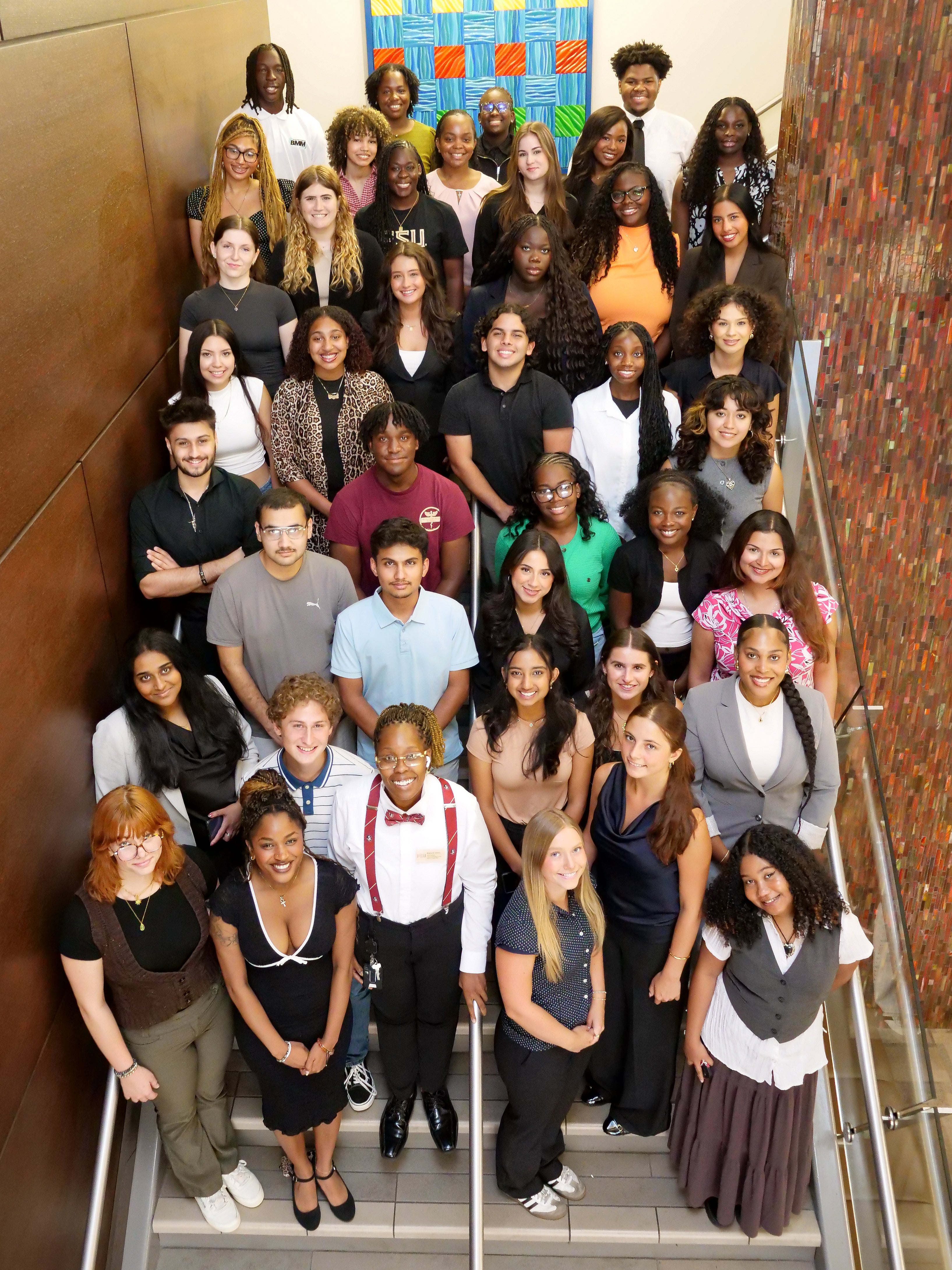 A group of more than 30 college students pose in rows up a flight of stairs looking up into camera.