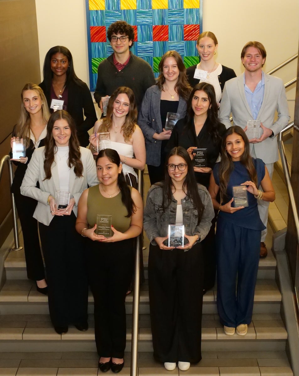 Twelve students holding plaques pose in rows on stairs.