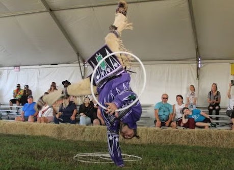 Indigenous person balances on one hand while performing a cultural dance.