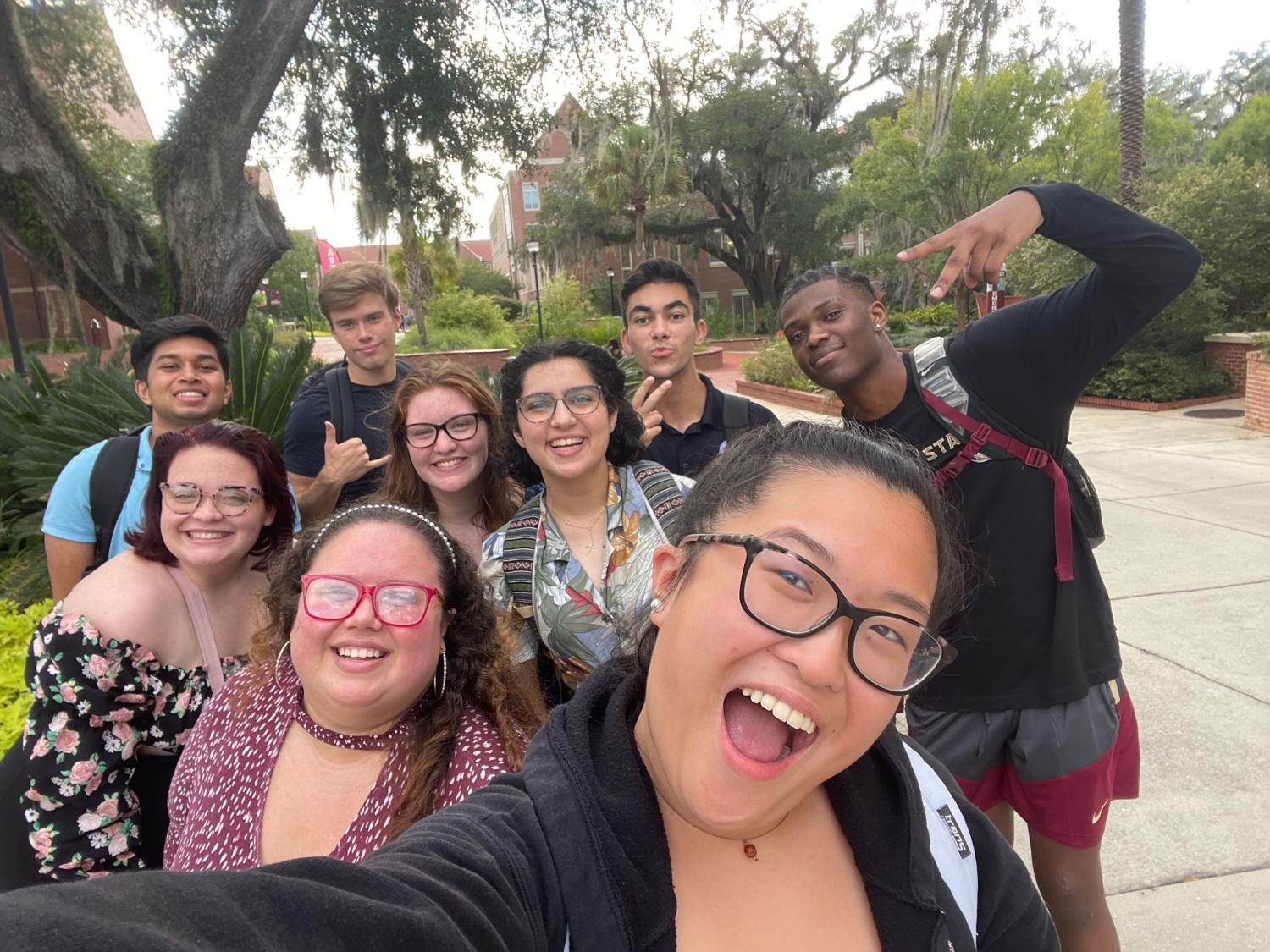 A group selfie of students in various poses on a campus sidewalk