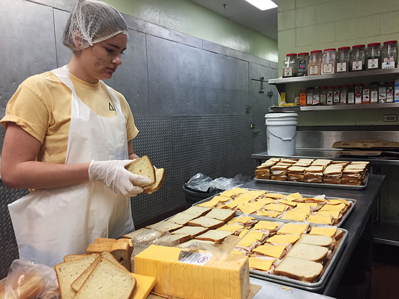 Student in hairnet preparing sandwiches.