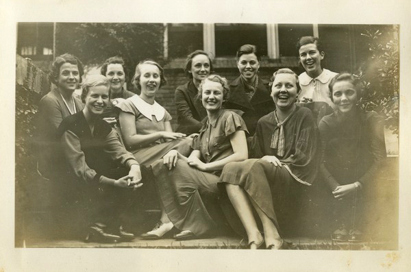 A group of twelve women sit laughing on steps outside of a building at the Florida State College for Women in the 1930s.