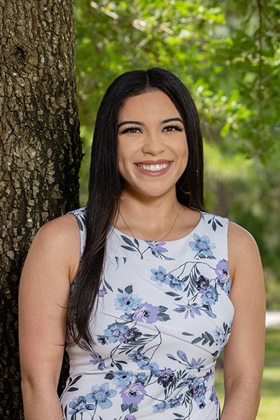 Portrait of Guissella E.Cruz Rodriguez leaning against a tree on campus