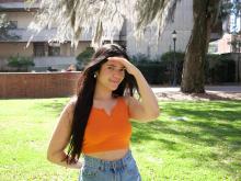 Girl with brown hair in an orange shirt smiling at the camera.